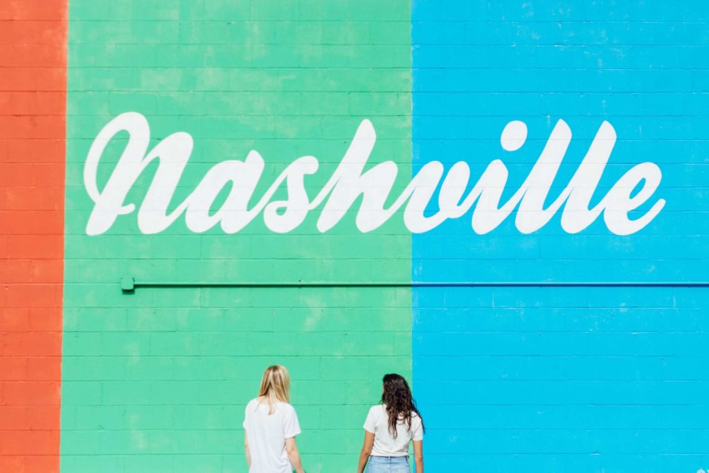 Two girls standing in front of colorful wall with "Nashville" painted in white text